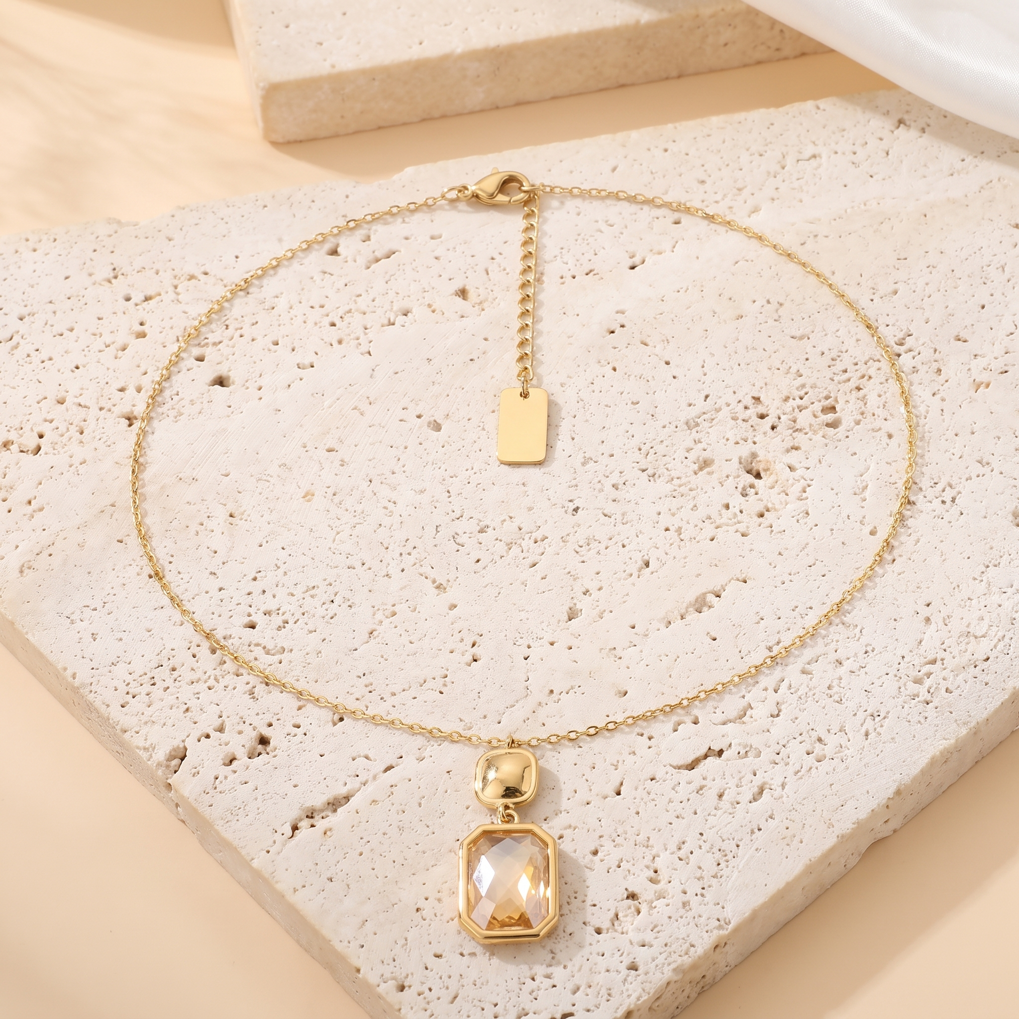Collier Halo en acier inoxydable doré, pendentif octogonal champagne sur maillon nugget, packshot sur travertin ivoire, Maison Sveltesse