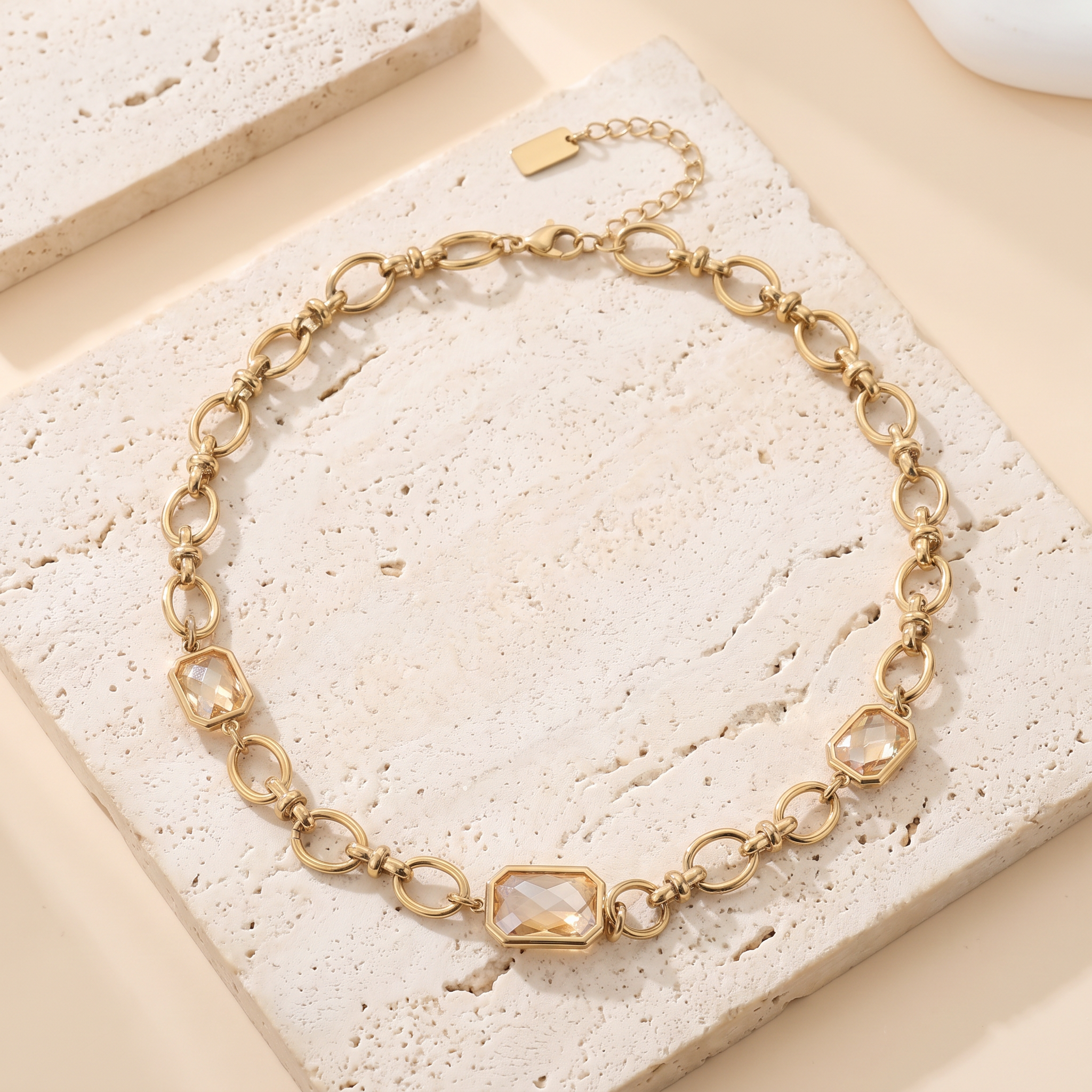 Collier Zénith en acier inoxydable doré, gros maillons et 3 stations pierres champagne, packshot sur travertin ivoire, Maison Sveltesse