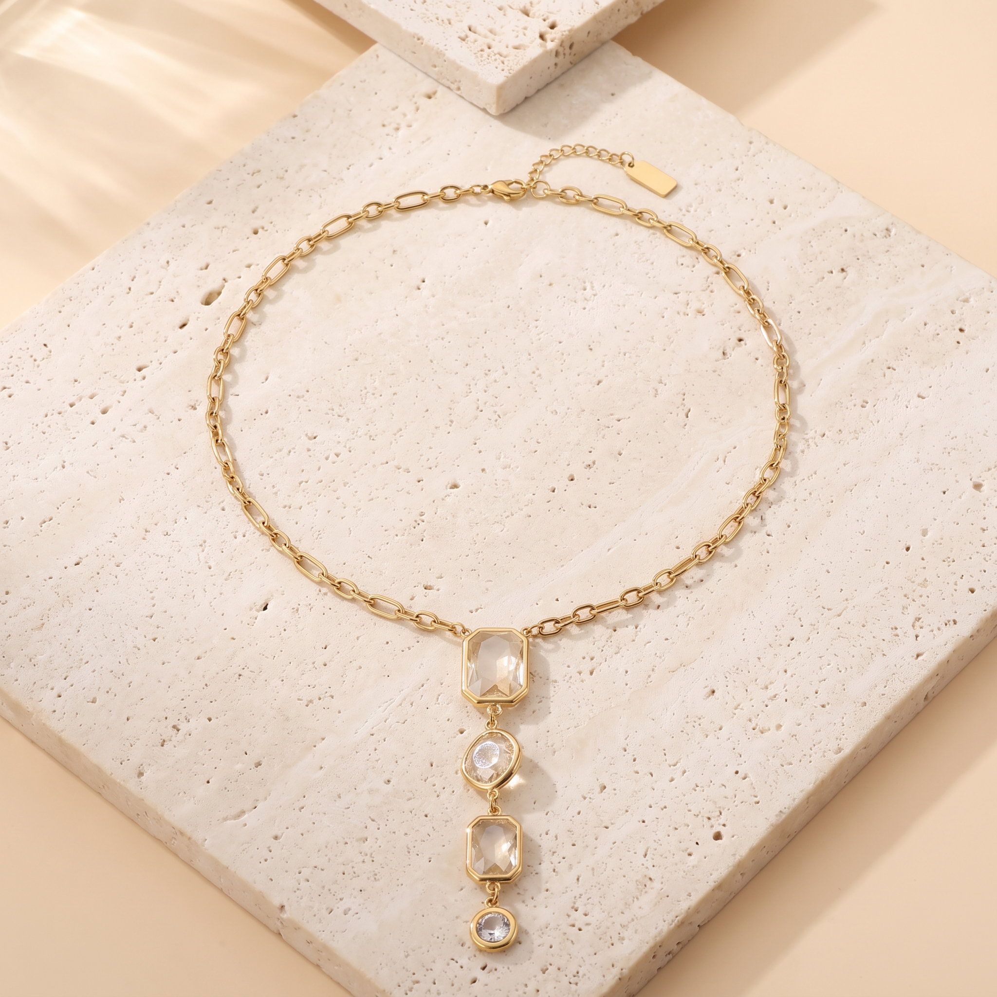 Collier Solstice Champagne en acier inoxydable doré, chaîne figaro chute en Y pierres champagne, packshot sur travertin ivoire, Maison Sveltesse