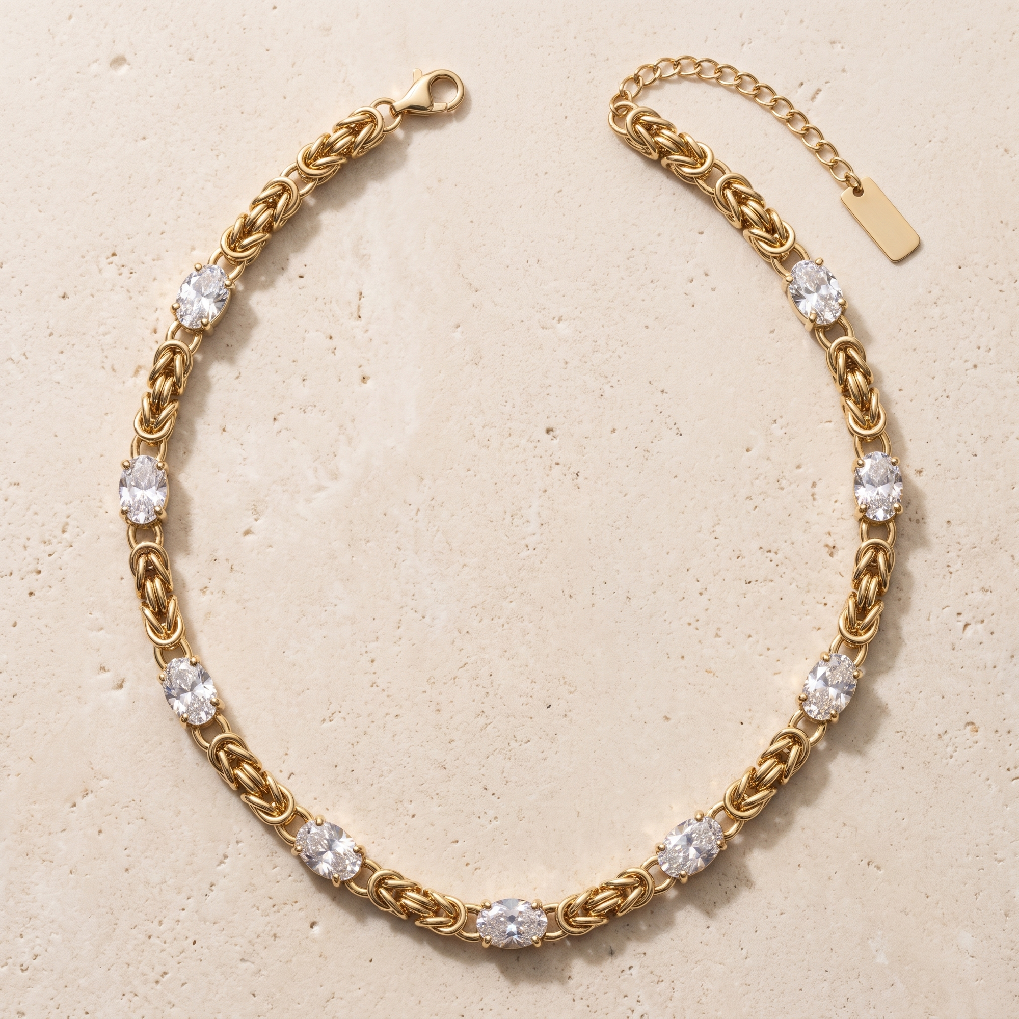 Collier Minuit en acier inoxydable doré, maille byzantine 8 stations cristal ovale, packshot sur travertin ivoire, Maison Sveltesse