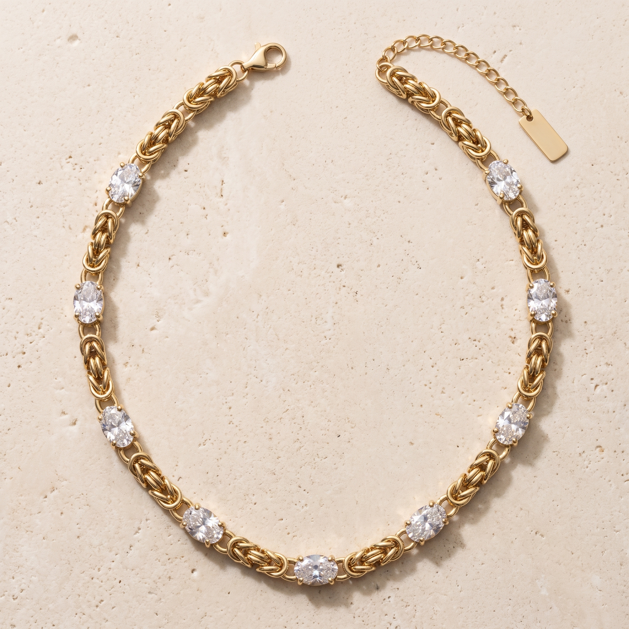 Collier Minuit en acier inoxydable doré, maille byzantine 8 stations cristal ovale, packshot sur travertin ivoire, Maison Sveltesse