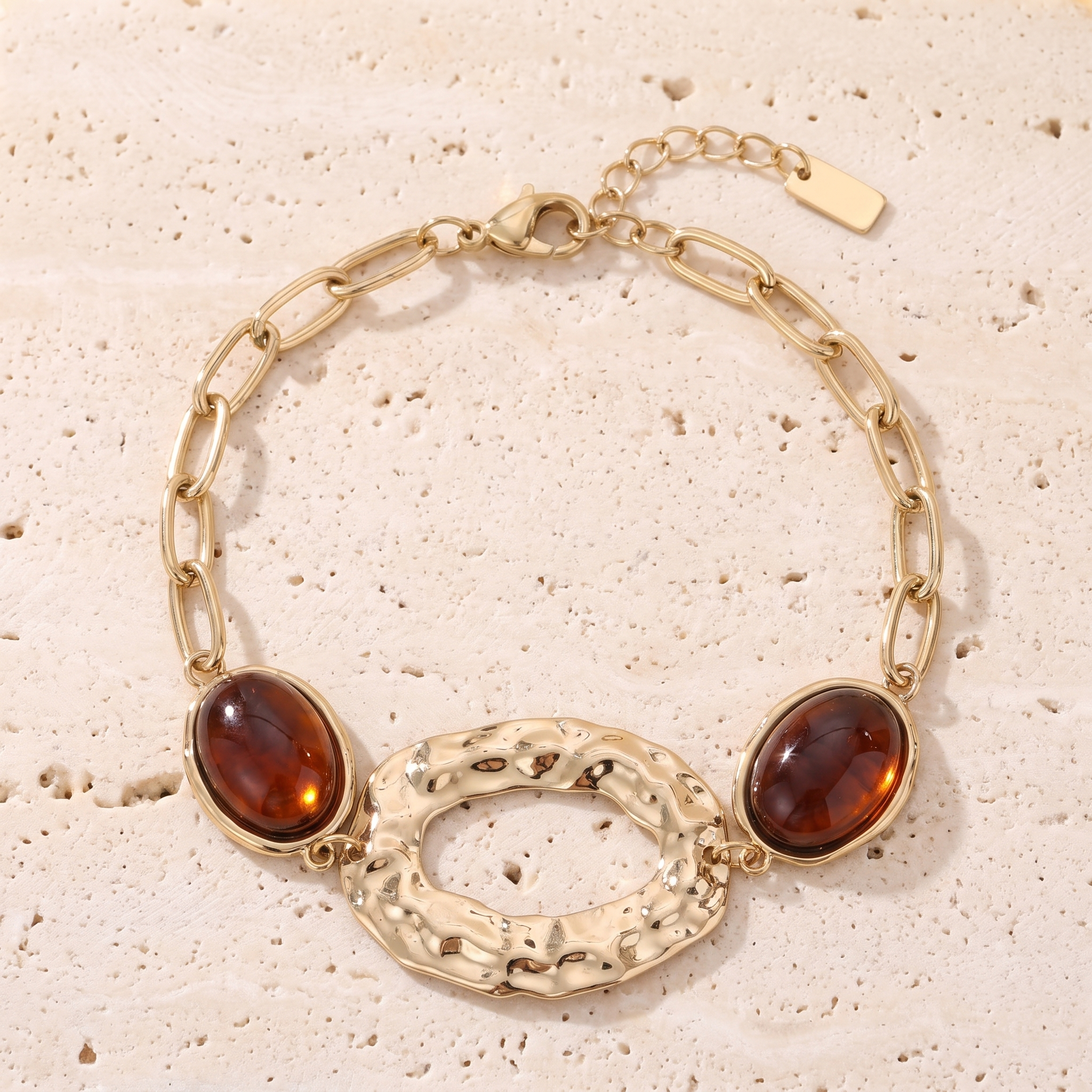 Bracelet Comète en acier inoxydable doré, anneau martelé et cabochons cognac, packshot sur travertin ivoire, Maison Sveltesse