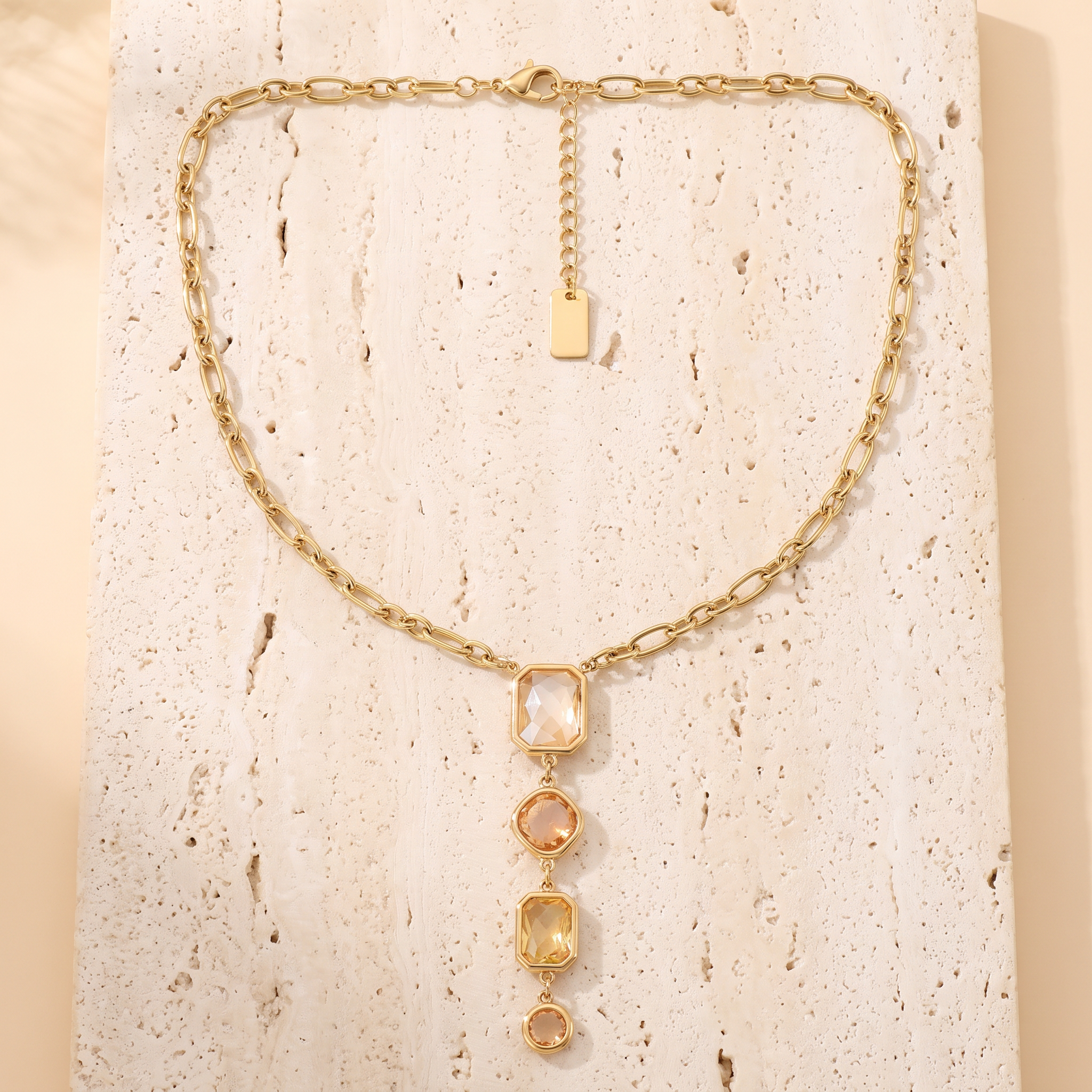 Collier Solstice Ambre en acier inoxydable doré, chute en Y dégradé champagne, packshot sur travertin ivoire, Maison Sveltesse