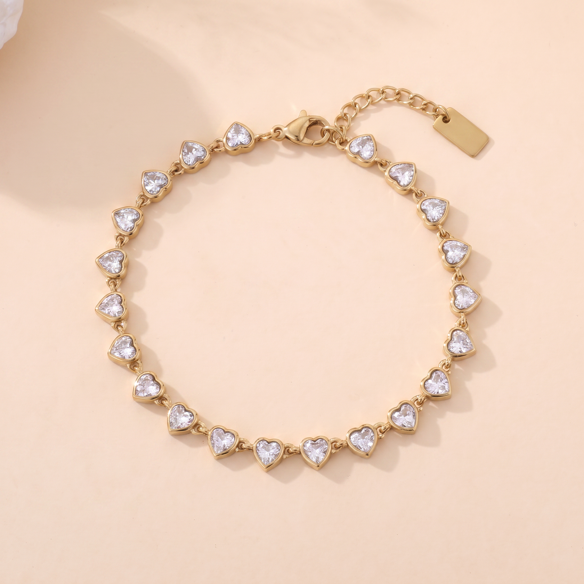 Bracelet Éclipse en acier inoxydable doré, rivière de cœurs en cristal incolore, packshot sur travertin ivoire, Maison Sveltesse