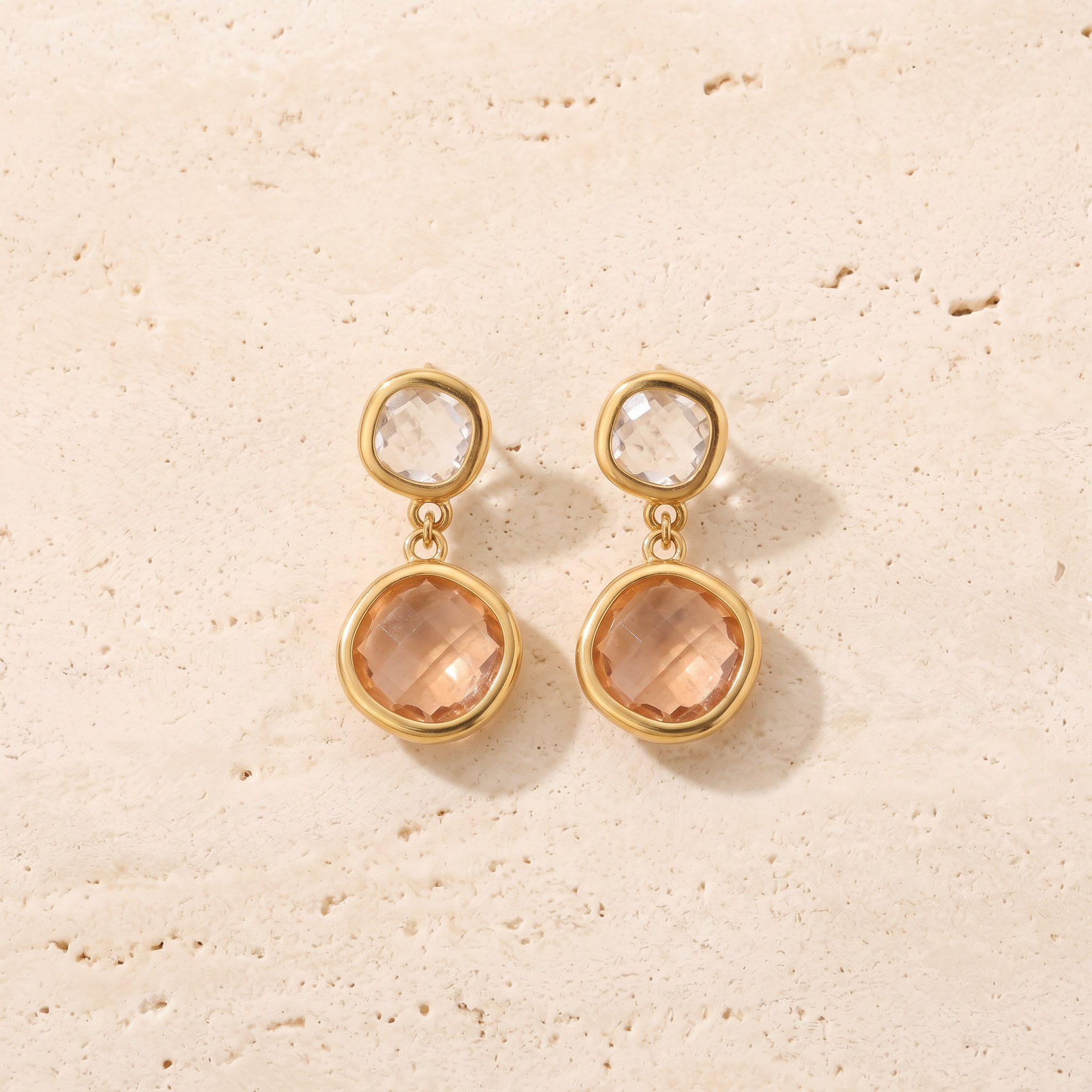 Boucles Crépuscule en acier inoxydable doré, puce incolore et pierre pêche abricot, packshot sur travertin ivoire, Maison Sveltesse