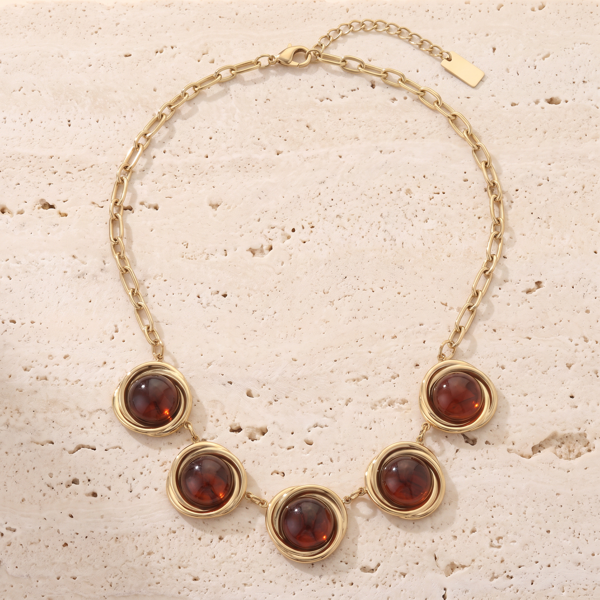 Collier Couchant Cognac en acier inoxydable doré, 5 cabochons cognac et anneaux torsadés, packshot sur travertin ivoire, Maison Sveltesse