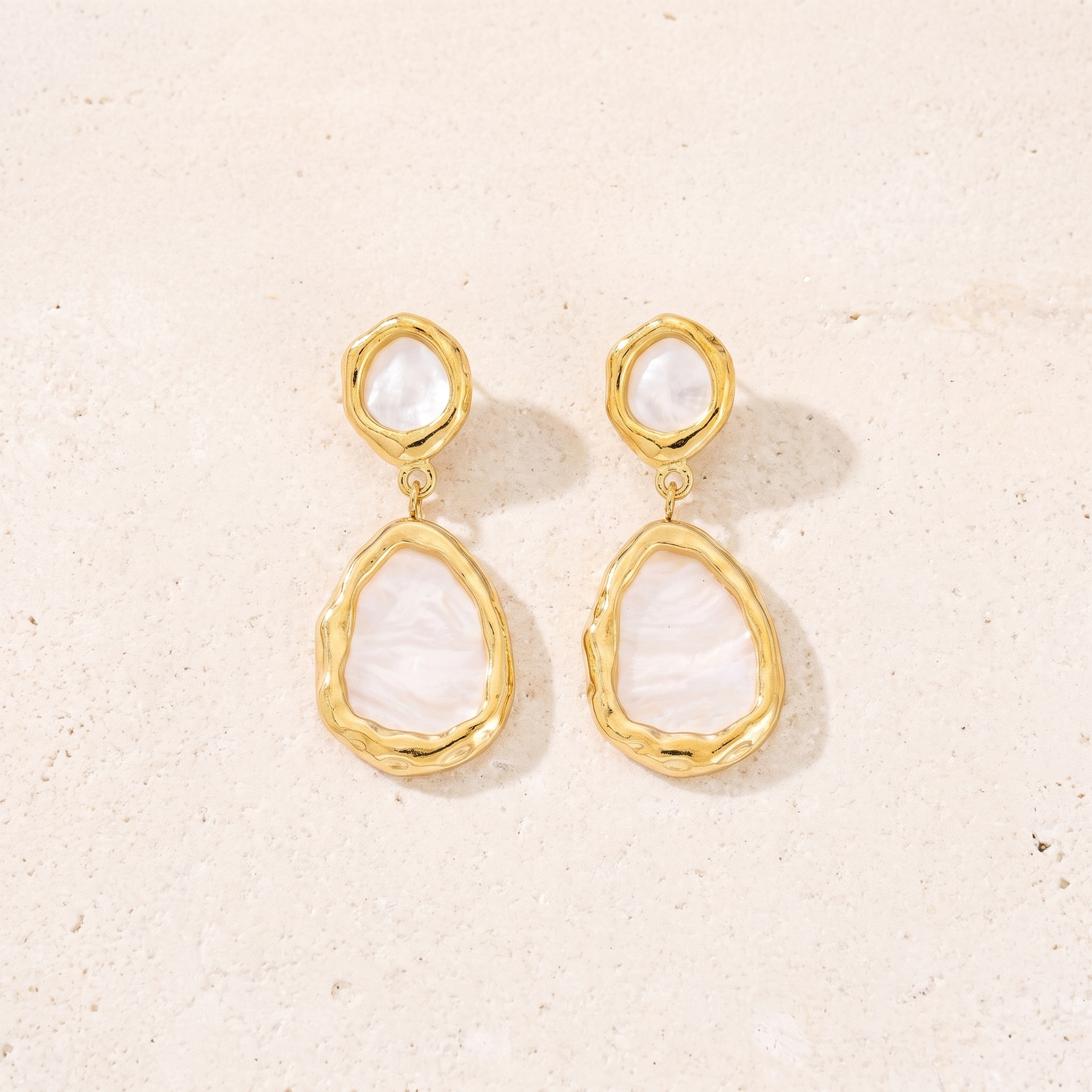Boucles Sélène en acier inoxydable doré, nacre blanche et cadres martelés, packshot sur travertin ivoire, Maison Sveltesse