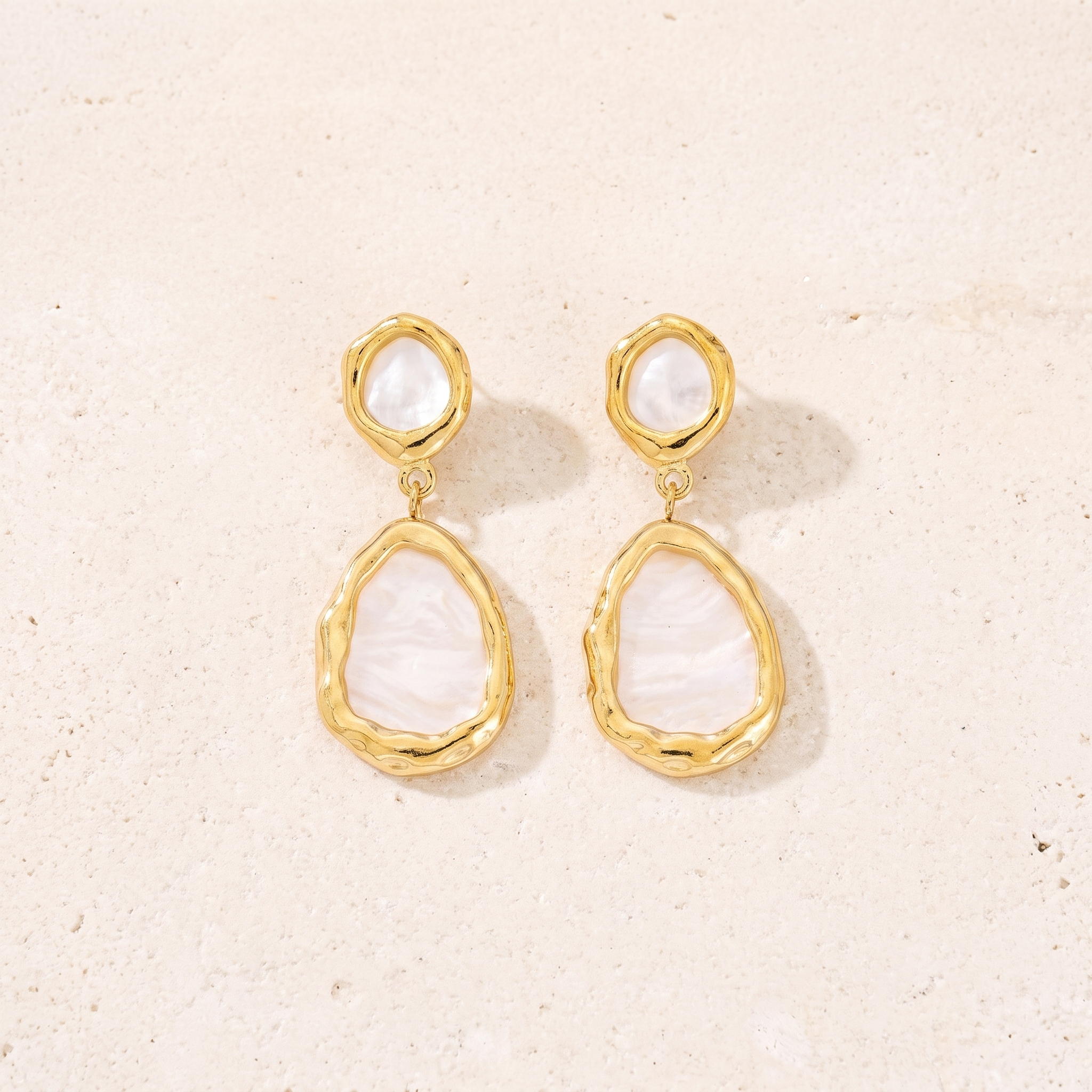 Boucles Sélène en acier inoxydable doré, nacre blanche et cadres martelés, packshot sur travertin ivoire, Maison Sveltesse