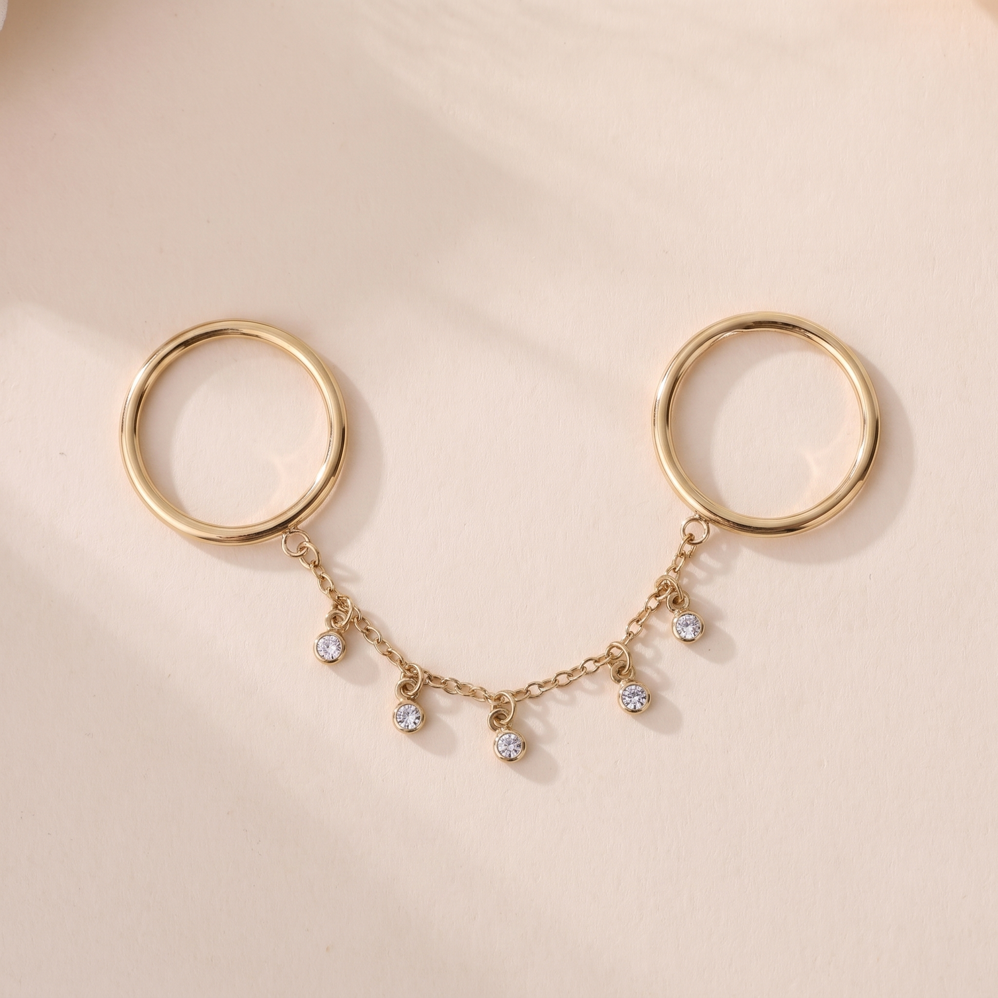 Bague Nova en acier inoxydable doré, deux anneaux reliés par une chaîne à six pampilles cristal, packshot sur travertin ivoire, Maison Sveltesse
