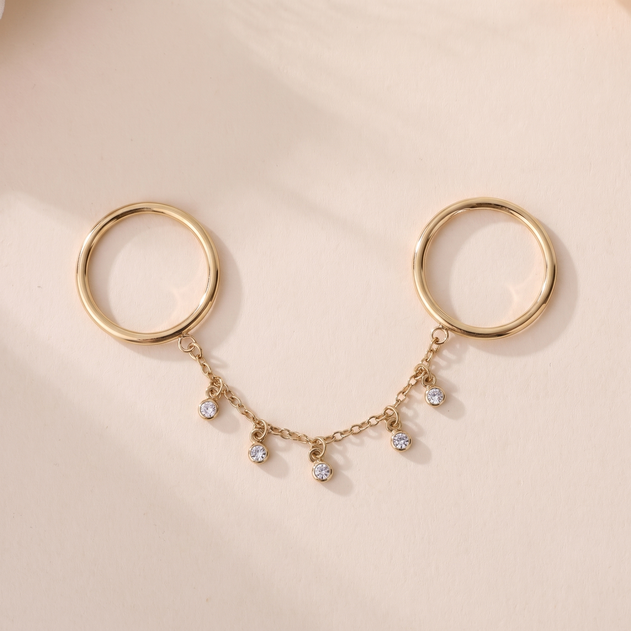 Bague Nova en acier inoxydable doré, deux anneaux reliés par une chaîne à six pampilles cristal, packshot sur travertin ivoire, Maison Sveltesse