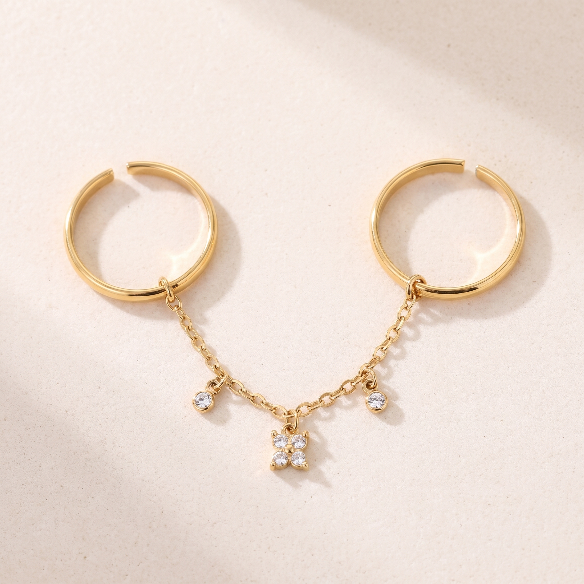 Bague Véga en acier inoxydable doré, anneaux ouverts ajustables, fleur cristal et chaîne à trois pampilles, packshot sur travertin ivoire, Maison Sveltesse