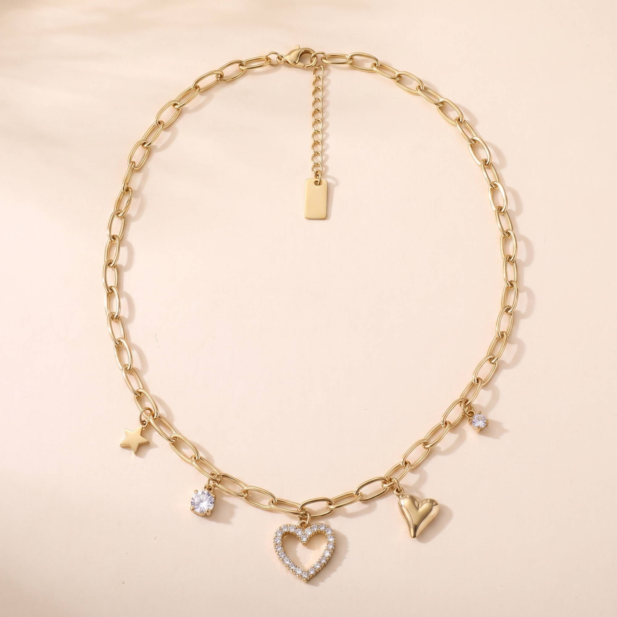 Collier Constellation en acier inoxydable doré, 5 breloques étoile et cœurs, packshot sur travertin ivoire, Maison Sveltesse