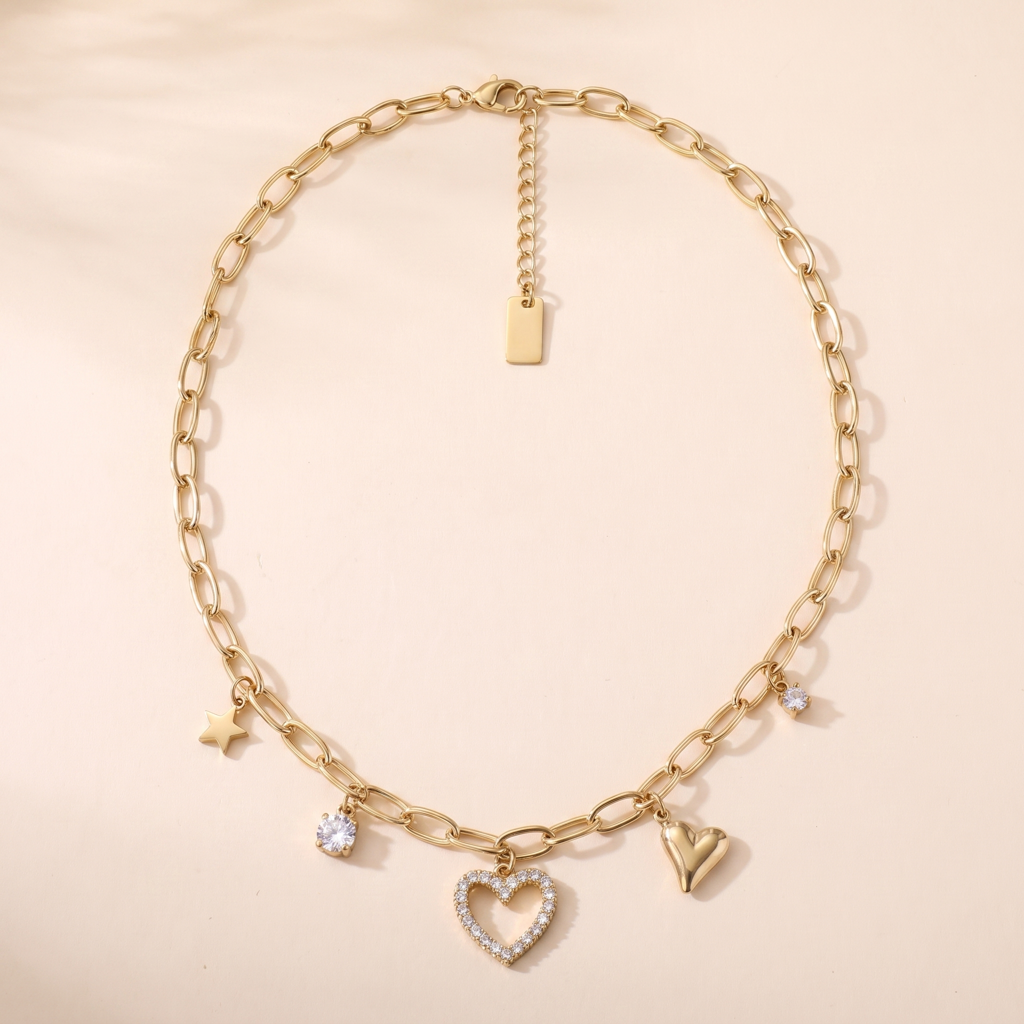 Collier Constellation en acier inoxydable doré, 5 breloques étoile et cœurs, packshot sur travertin ivoire, Maison Sveltesse