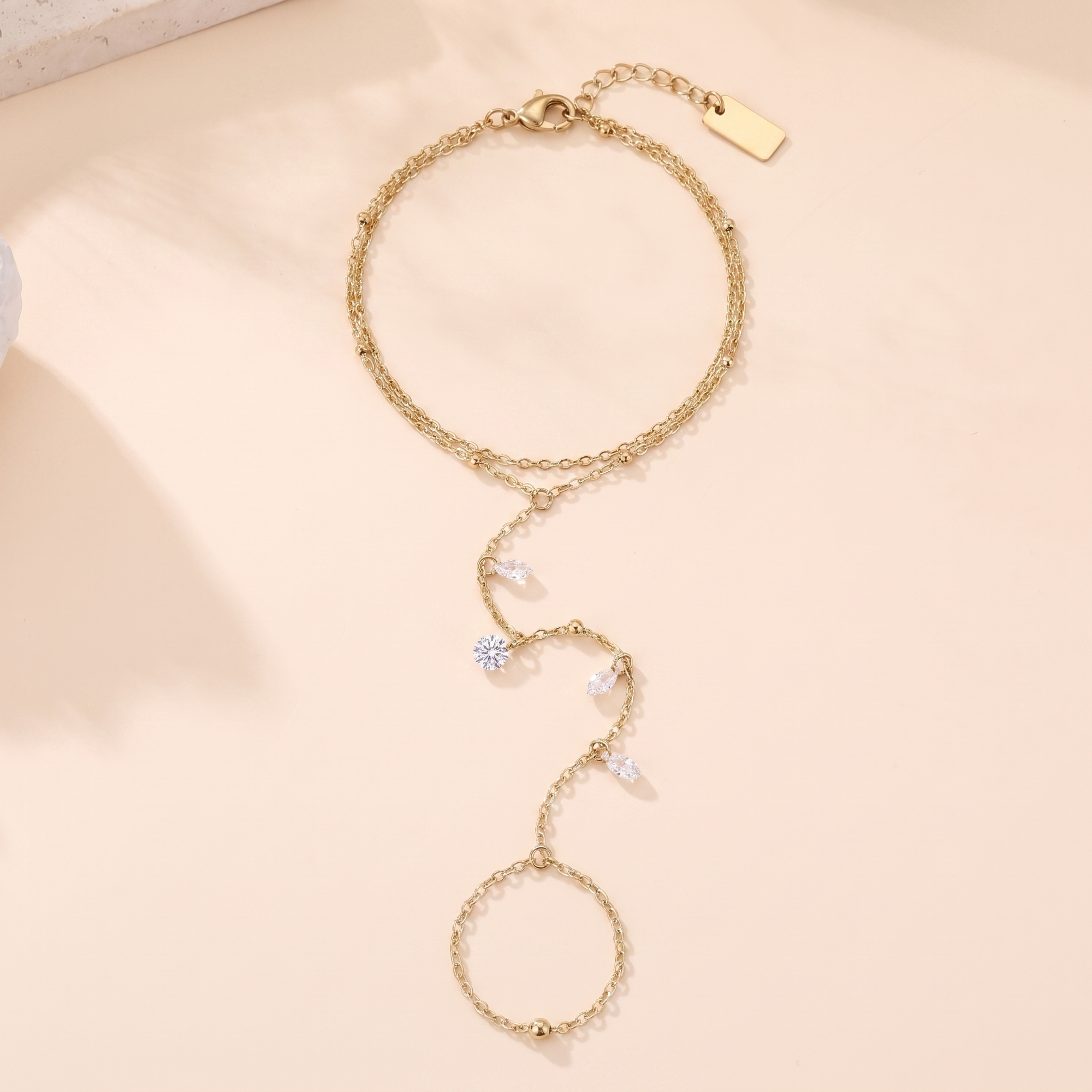Chaîne de main Aurore en acier inoxydable doré, double rang et quatre pierres, packshot sur travertin ivoire, Maison Sveltesse