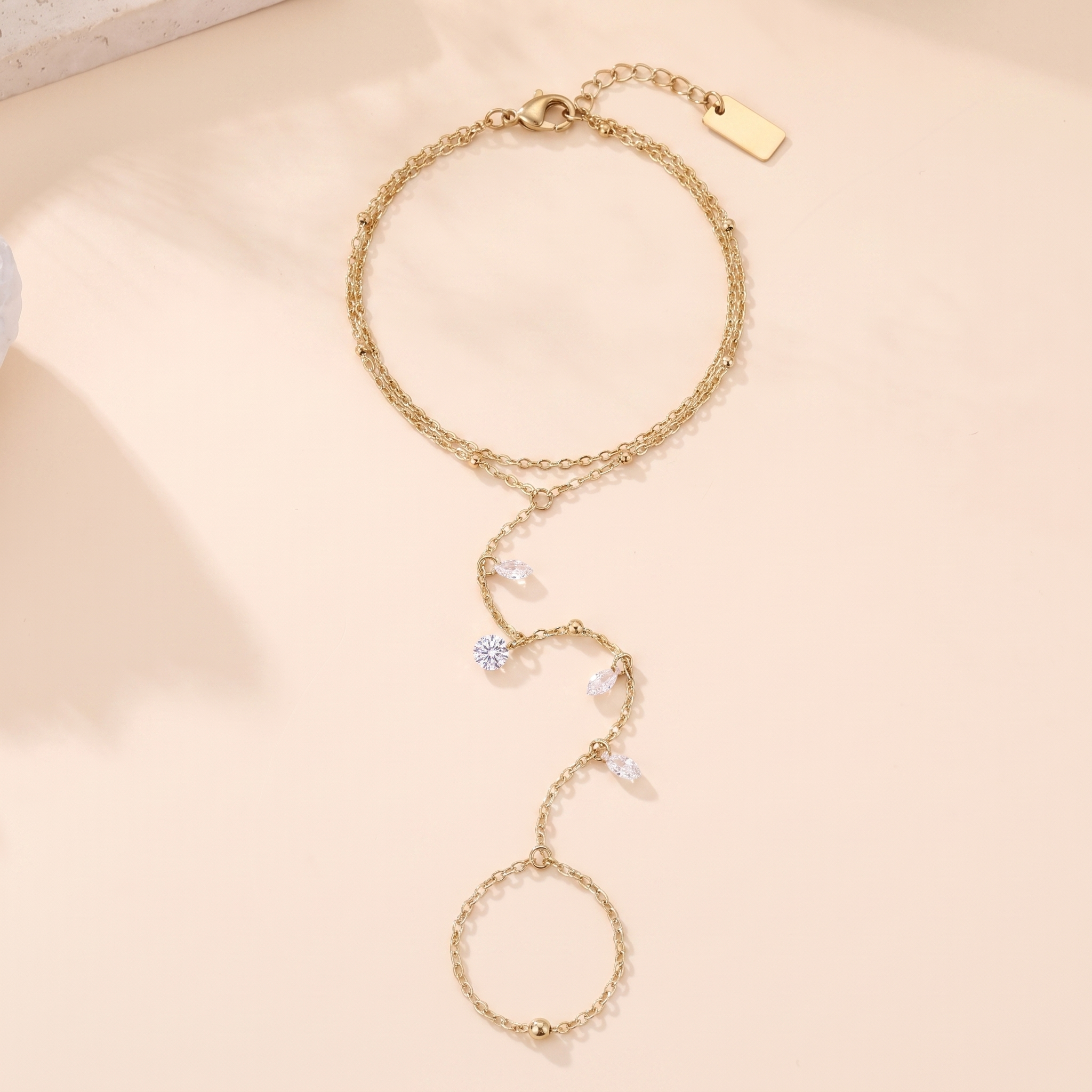 Chaîne de main Aurore en acier inoxydable doré, double rang et quatre pierres, packshot sur travertin ivoire, Maison Sveltesse