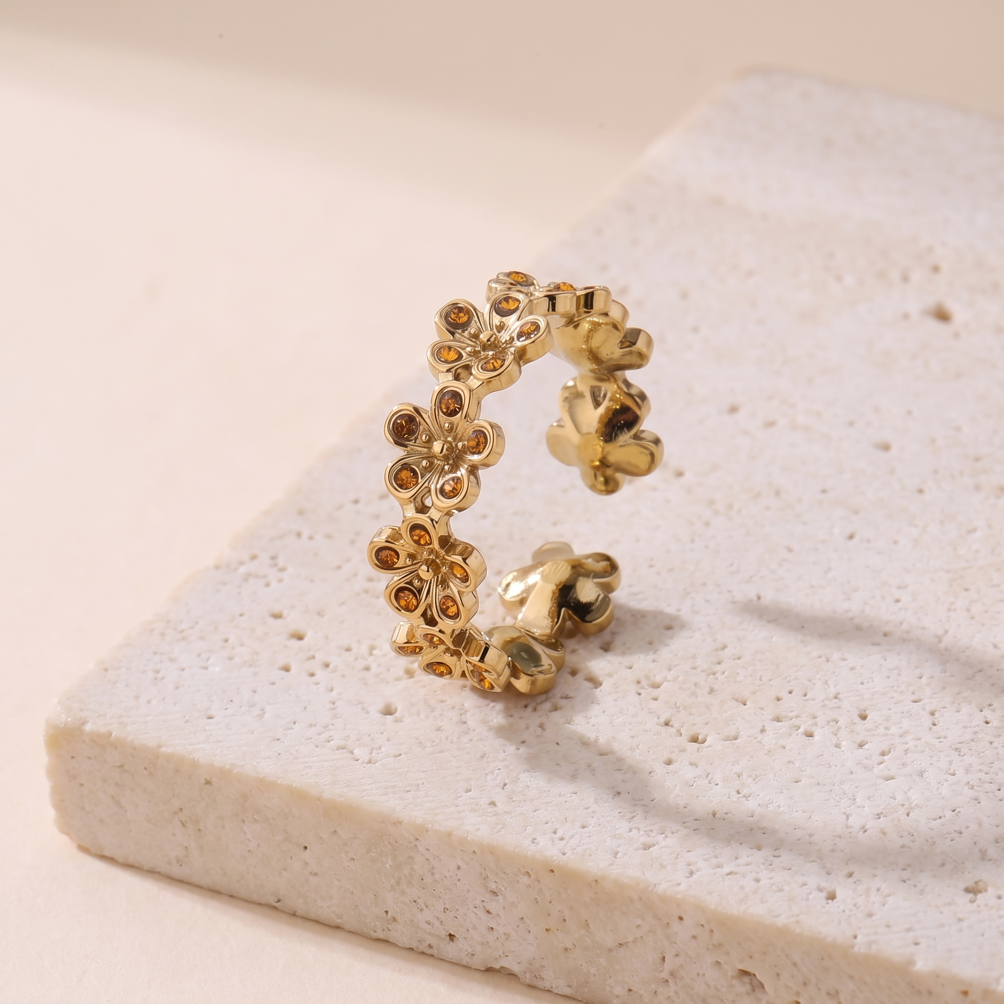Bague Couronne en acier inoxydable doré, guirlande de marguerites serties de pierres cognac, packshot sur travertin ivoire, Maison Sveltesse
