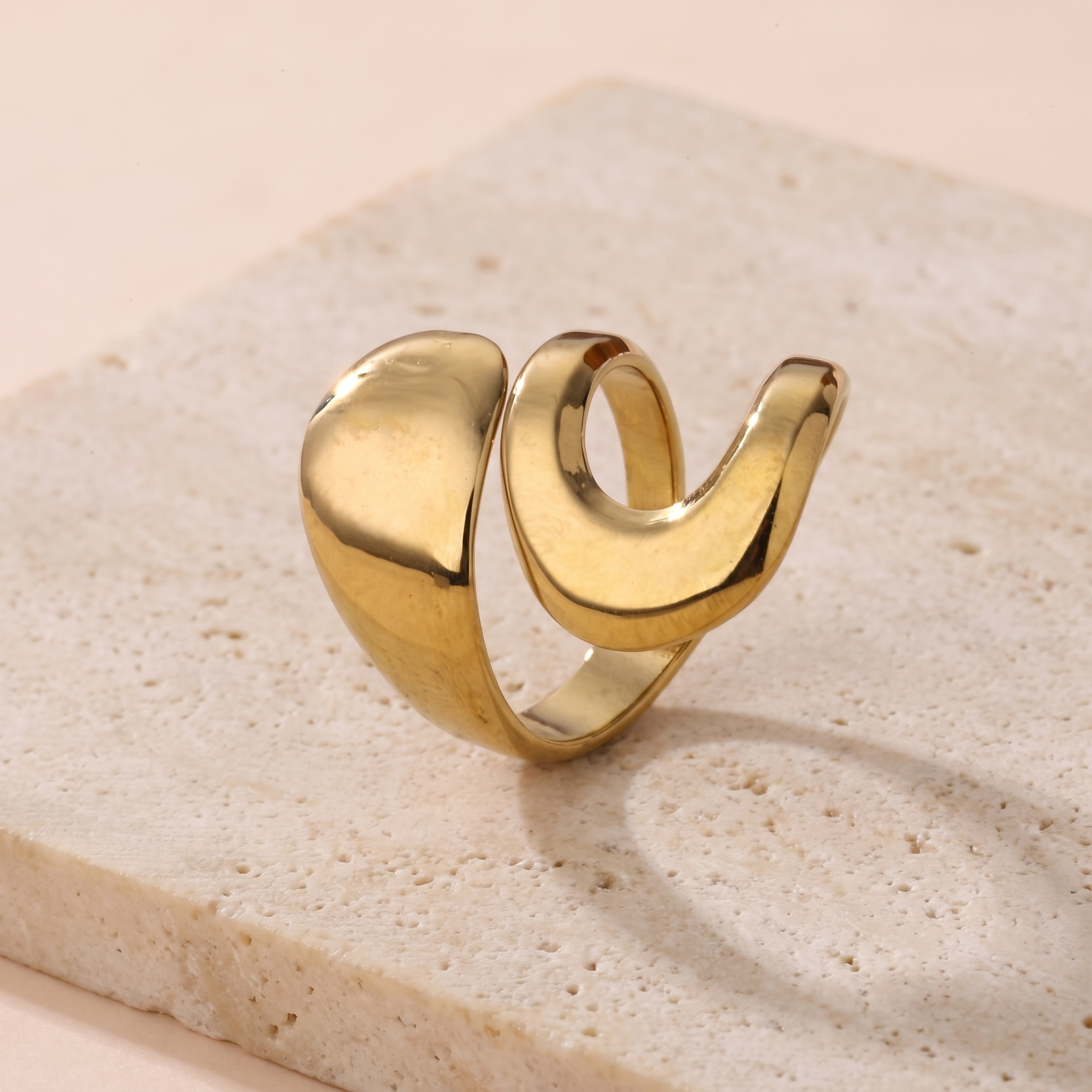 Bague Mercure en acier inoxydable doré, anneau sculptural ouvert poli miroir, packshot sur travertin ivoire, Maison Sveltesse