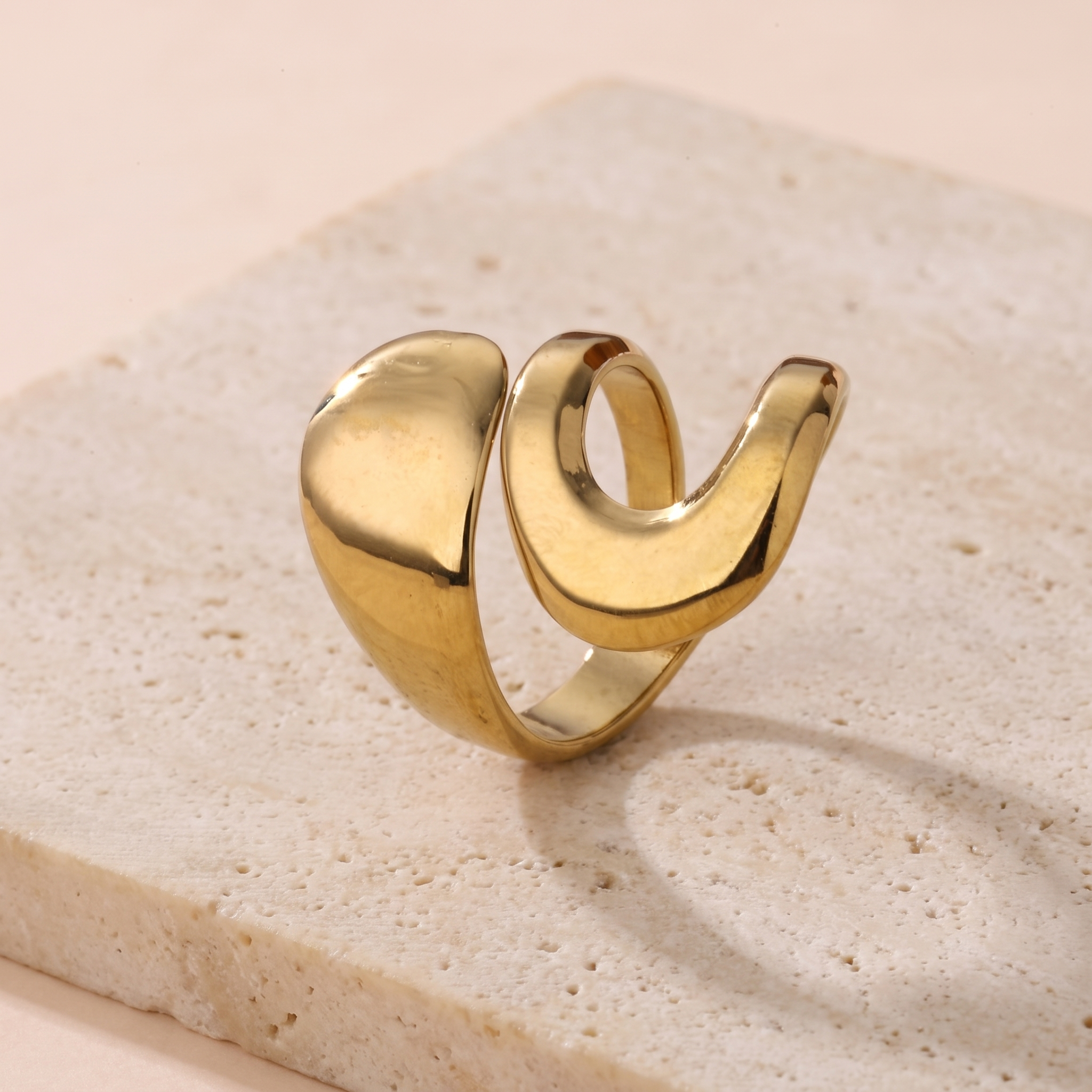 Bague Mercure en acier inoxydable doré, anneau sculptural ouvert poli miroir, packshot sur travertin ivoire, Maison Sveltesse
